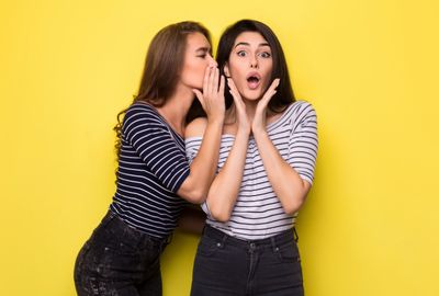 Two women whispering marketing secrets involving promotional lapel pins.