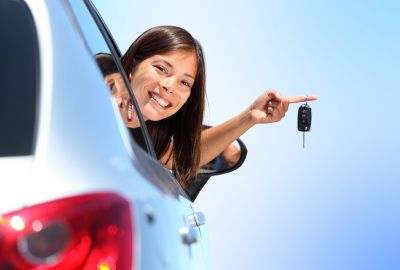 A new car owner proudly displaying their keys with custom metal keyring while leaning out of the car window.