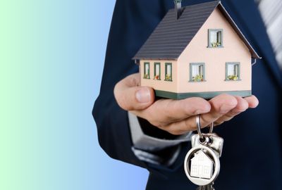 A realtor holding a model home and a custom metal keychain.