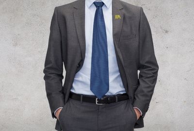 A man wearing a suit with an all metal lapel pin attached to it.